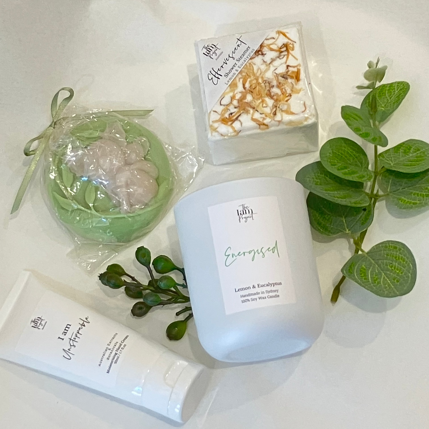 Candle, soap, and bath bomb with greenery on a white surface