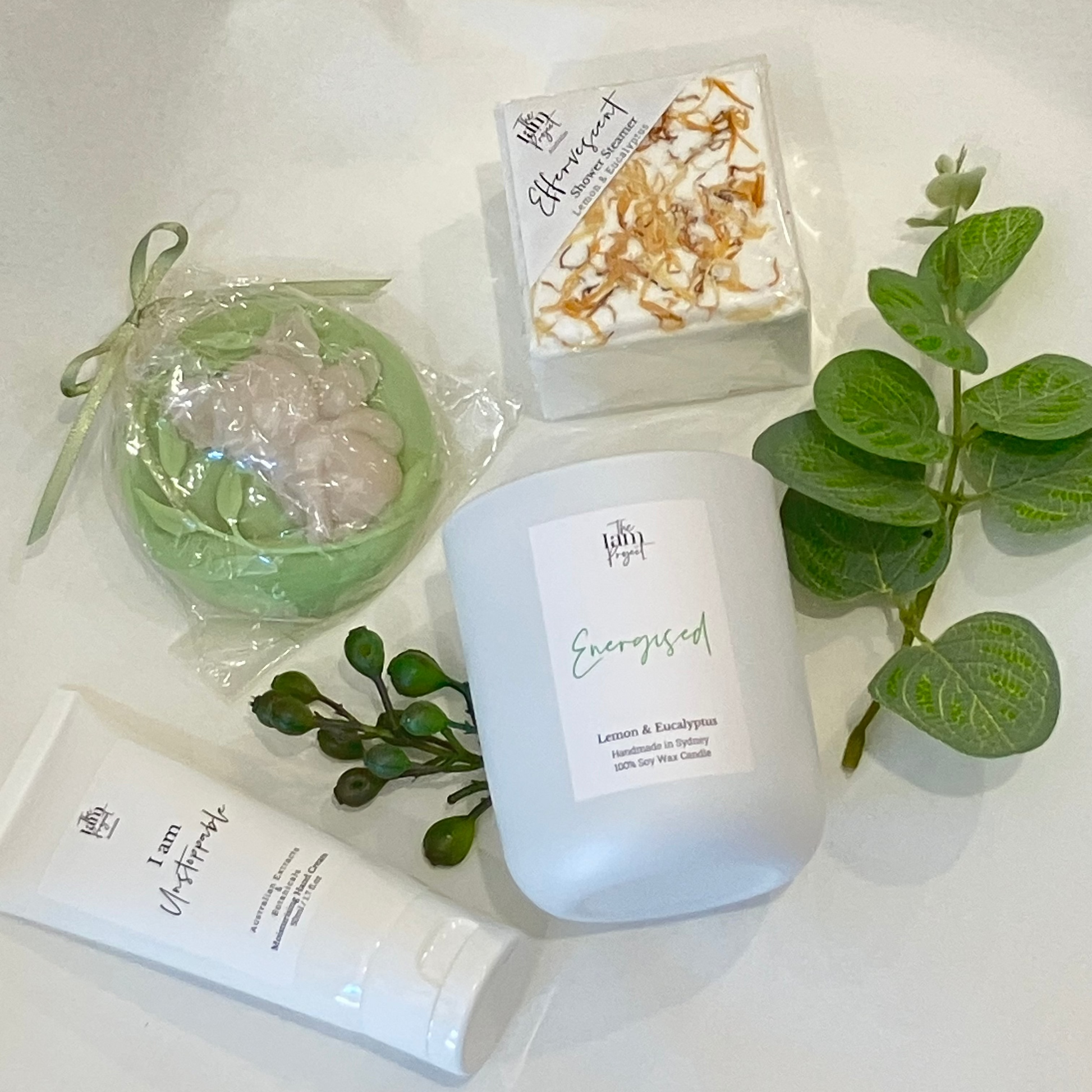 Candle, soap, and bath bomb with greenery on a white surface