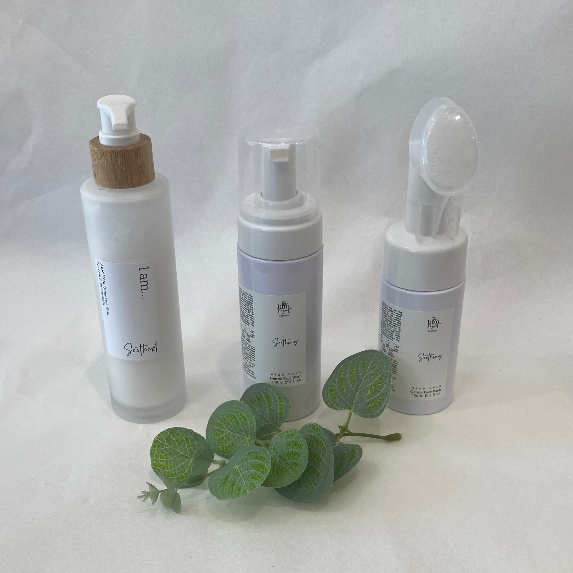 Three skincare bottles with a small green leaf on a white fabric background