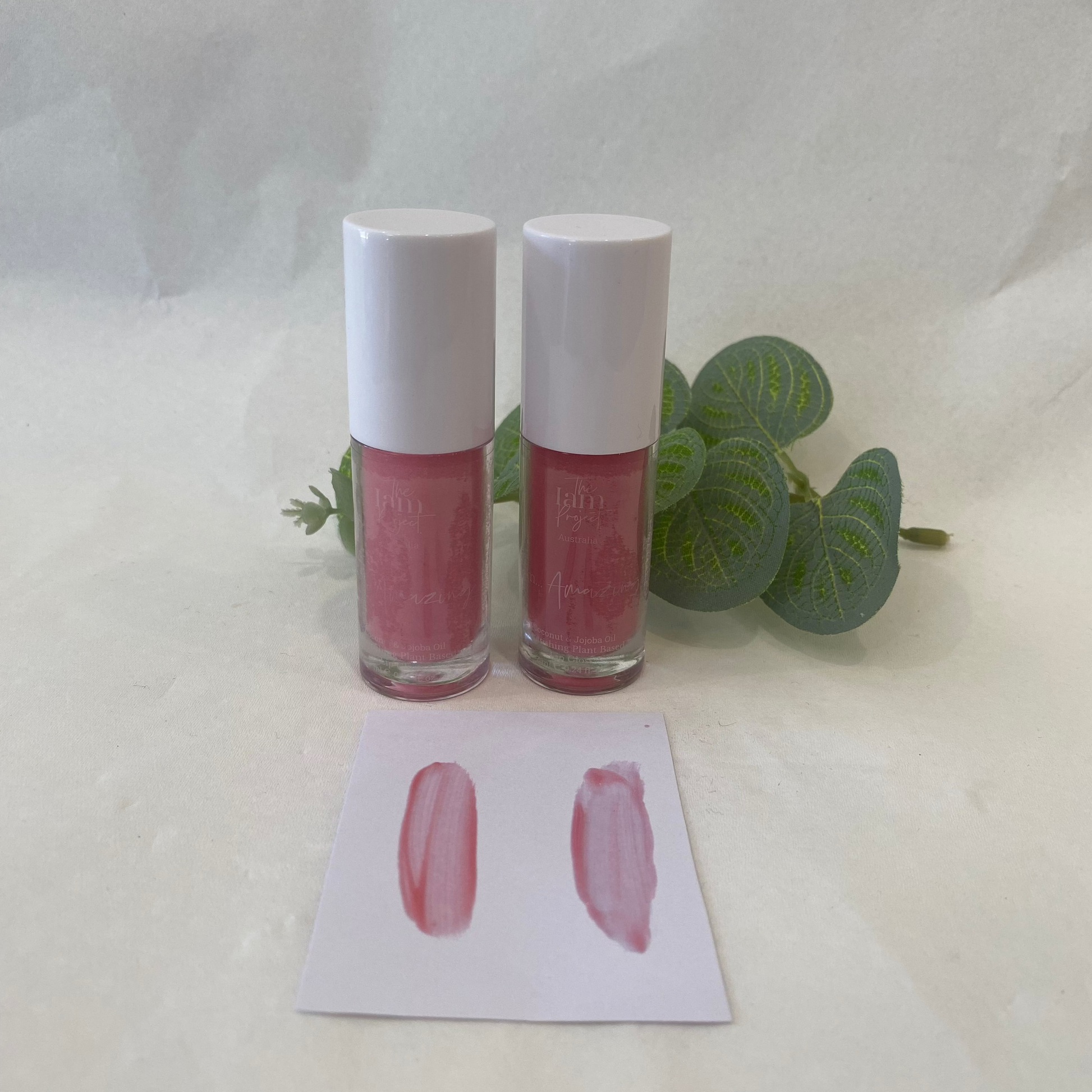 Two lip gloss bottles with a swatch on a white background
