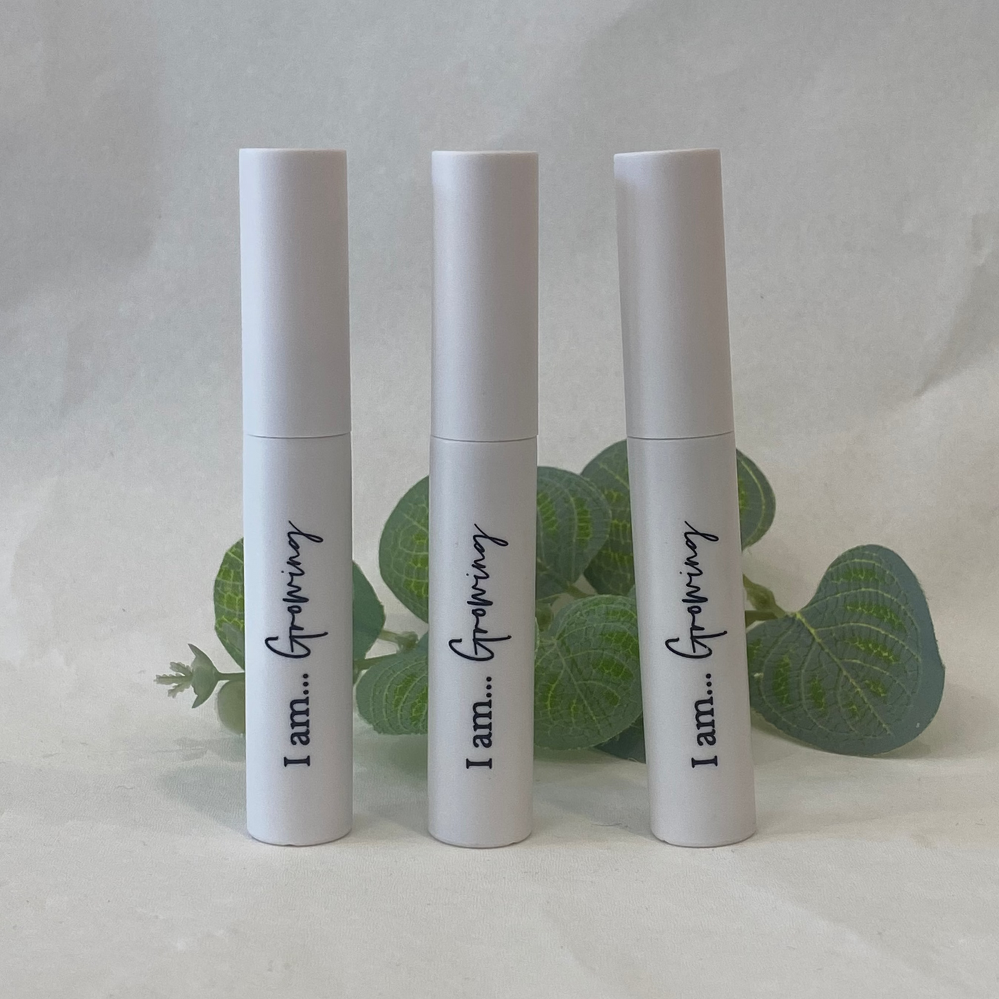 Three white Eyelash Serum bottles with text on a light background