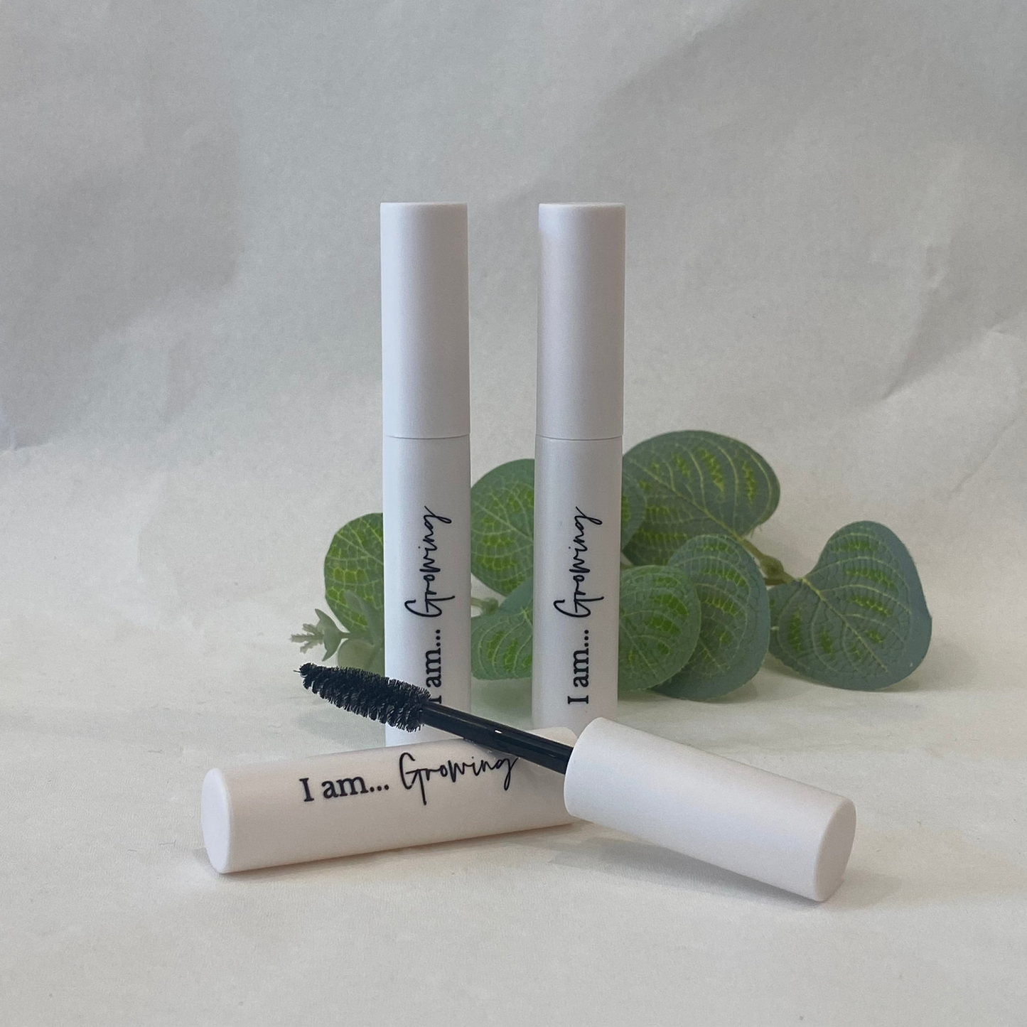 Three white mascara tubes with black lashes on a light gray background