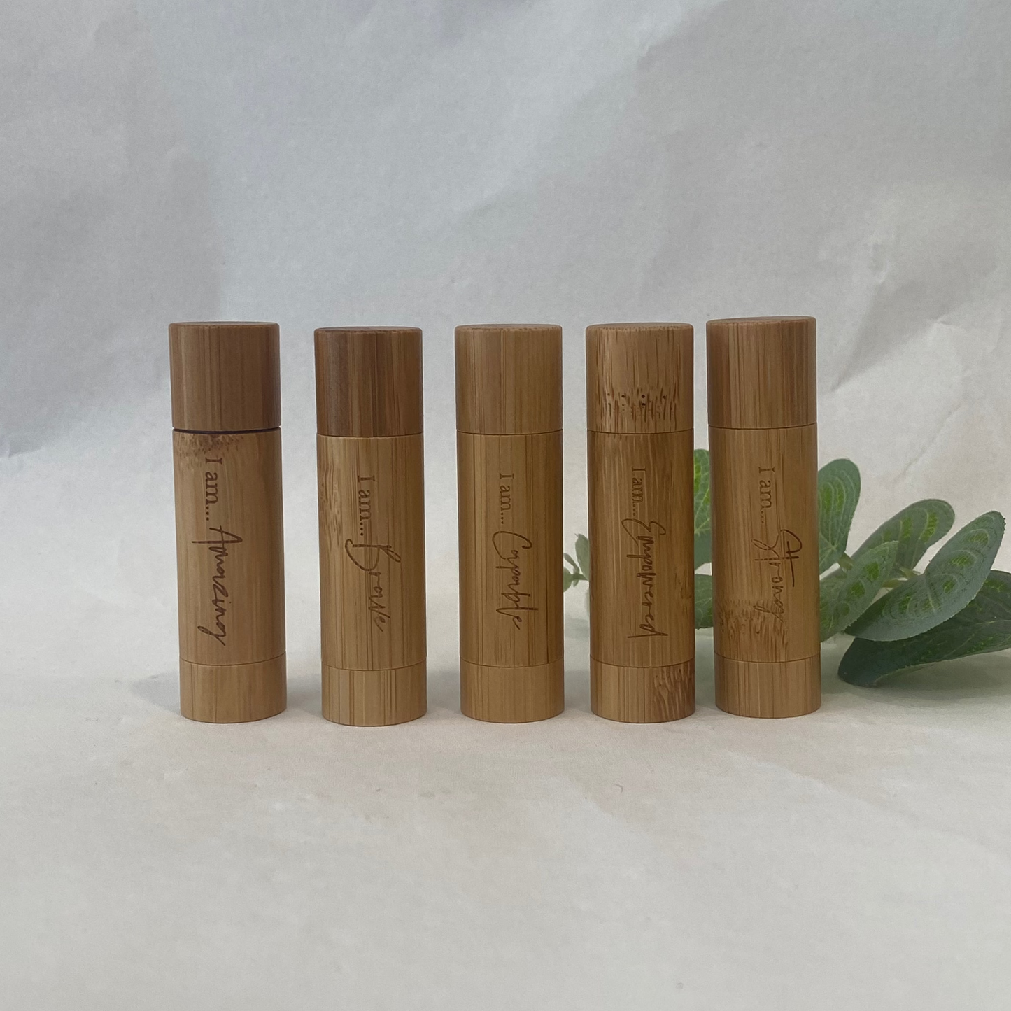 Five wooden lip balm tubes with engraved text on a white background