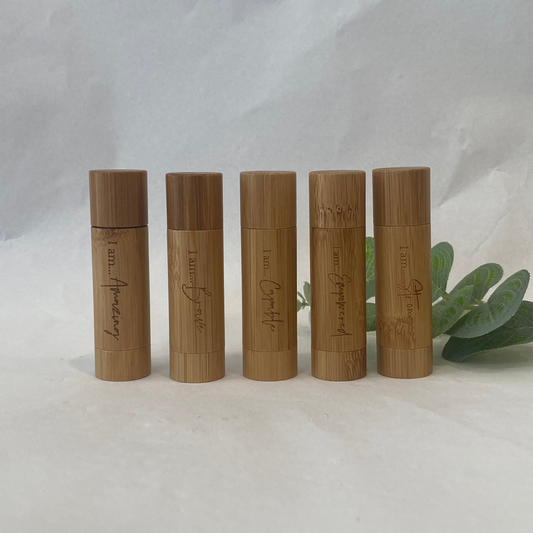 Five wooden lip balm tubes with engraved text on a white background