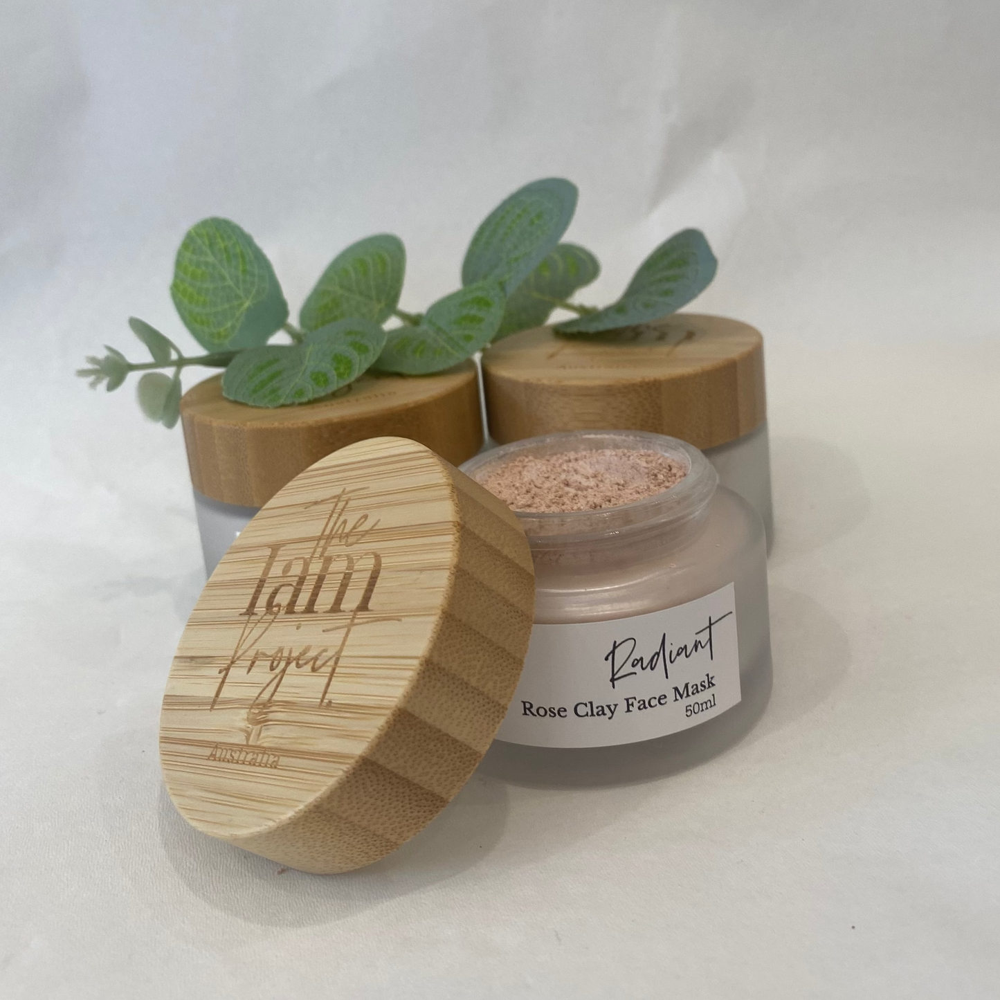 Rose clay face mask in a glass jar with a wooden lid on a white background
