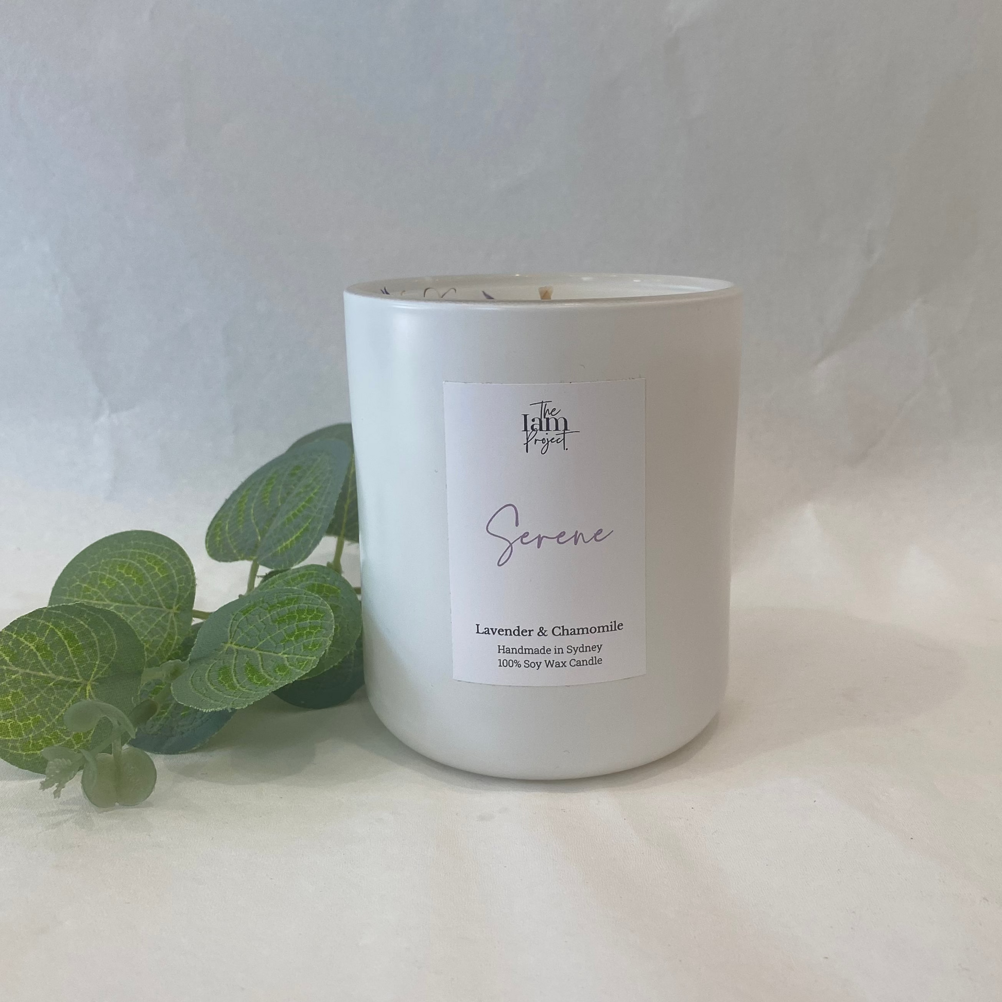 White candle labeled 'Serenity' with green leaves on a white background