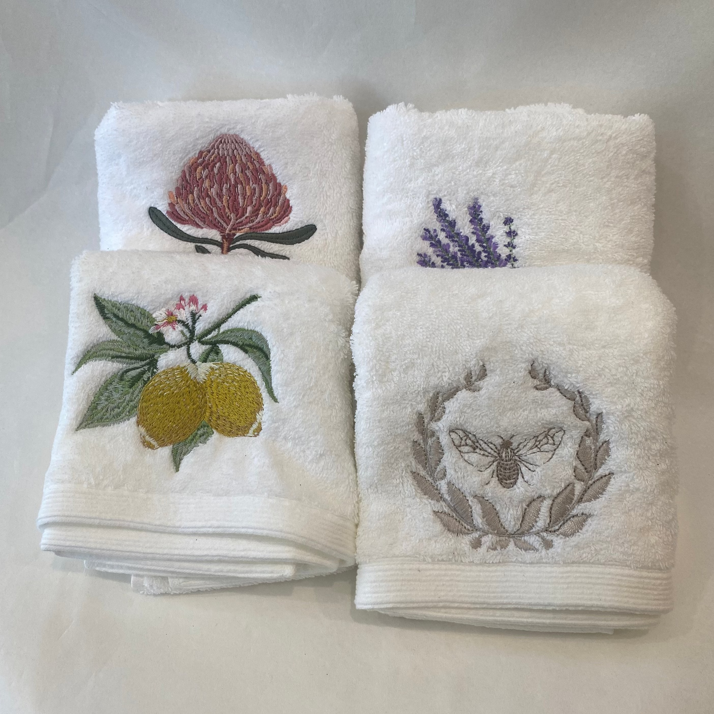 Set of four white towels with embroidered designs on a white background