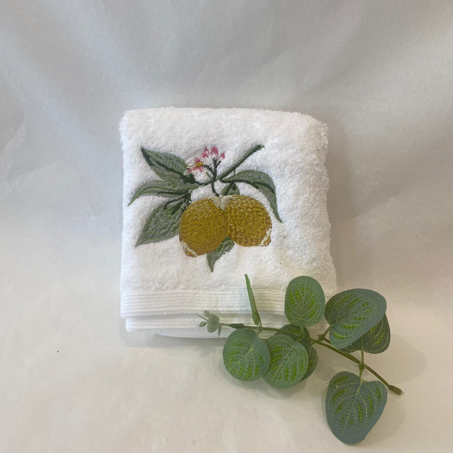 White hand towel with embroidered lemons and leaves on a white background